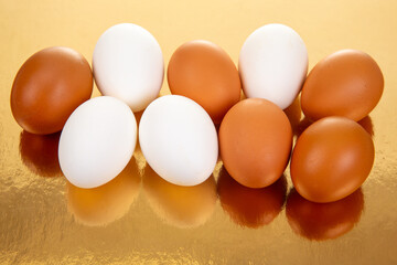 A row of white and brown eggs arranged neatly on a reflective golden surface, showcasing a warm and glossy food photography composition with soft shadows.