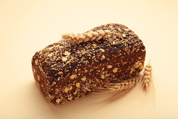 Wheat bread with mixed seeds and ears of wheat on beige background