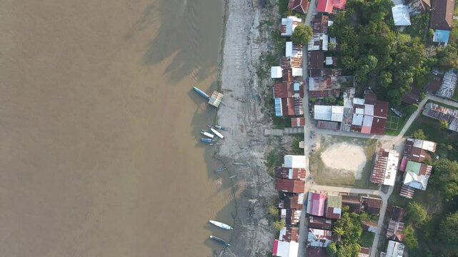 Aerial top down pan across riverside village, Iquitos, Peru, houses, boats, and muddy water flow at sunrise