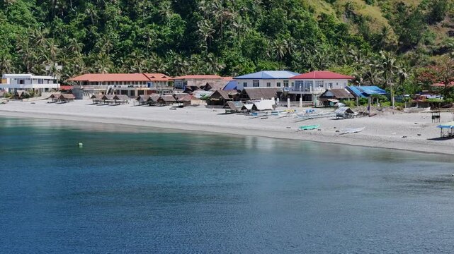 An expansive aerial shot of Looc Pebble Beach in Surigao City, Philippines, capturing sunlit cottages, pebbled shores, bustling fishing boats, and coastal resorts against a vibrant tropical backdrop.