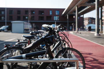 Selective focus at a row of bicycles is securely parked in a metal rack along a designated red cycling path in an urban environment. 