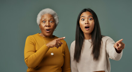 Surprised elderly african female and young asian female pointing forward
