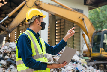 A waste management specialist in protective gear oversees a landfill site, ensuring compliance with...