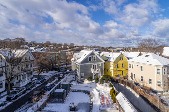 Aerial view of houses in Porter Square, MA, covered in winter snow with white clouds and blue sky in background