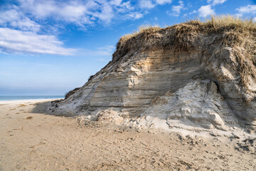 Rugged Coastal Sand Cliff with Grass Under Bright Blue Sky
