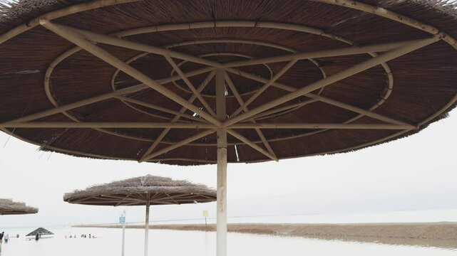 Parasol straw umbrella near sea shore. Straw umbrellas on hot summer day by beach. Sunny blue skies warm weather enjoyed on beach under parasol made of straw. Vacation in tropical countries