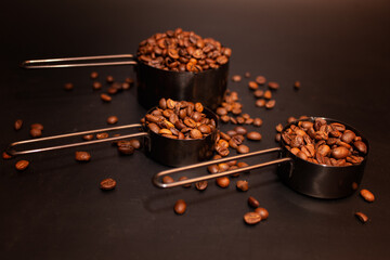 coffee beans roasted in measuring cups on a dark background scattered