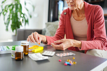 Senior woman organizing medications at home, carefully placing pills into a weekly pill organizer. Concept of elderly healthcare, daily medication routine, and independent living.