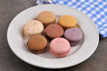 Assiette de macarons de différentes saveurs en gros plan à côté d'une serviette à carreaux sur fond gris
