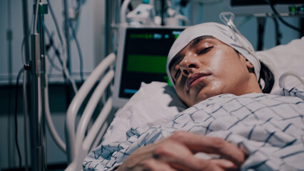 Unconscious patient lies motionless in hospital bed, his head wrapped in bandages. Medical monitors display vital signs of patient, emphasizing critical condition and advanced care in hospital setting