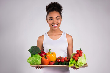 Black girl holding tray with vegetables isolated.
