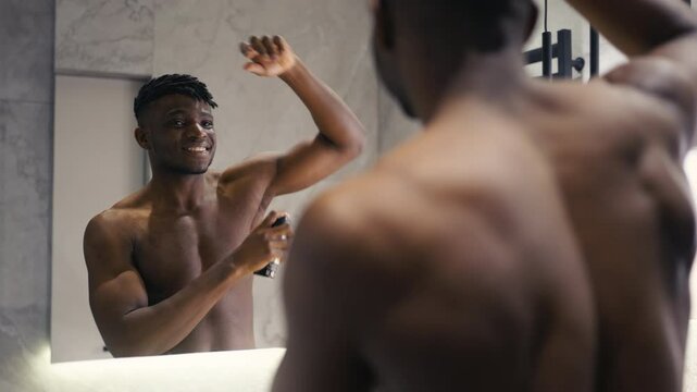 Fit African American male applying dry antiperspirant spray in front of a mirror
