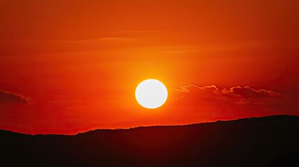 Fototapeta premium Majestic Mountain Sunset: Silhouette of the Sun atop Peaks, Red Sky with Clouds, Enhanced by Orange Tones and Backlighting, Captured with Telephoto Lens