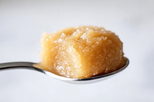 A spoonful of golden, textured cannabis concentrate, possibly honey oil or rosin.