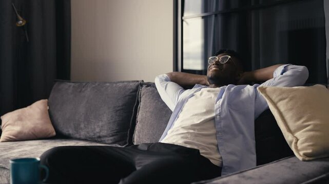 Young Black man sitting back and resting on the couch after a long workday