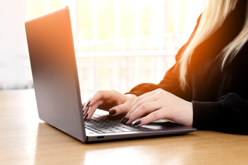 Young white caucasian woman working on computer on wooden table in home office. close up female businesswoman hands typing text on keyboard, surfing internet on modern laptop. mock up, top front view