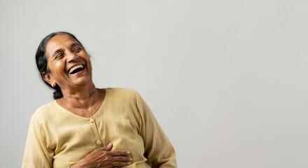 Obraz premium Joyful elderly asian female laughing in beige blouse against light background