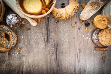 Bakery - various kinds of breadstuff. Bread rolls, baguette, bagel, sweet bun and croissant captured from above (top view, flat lay). wooden rustic background, copy space. Horizontal banner layout.