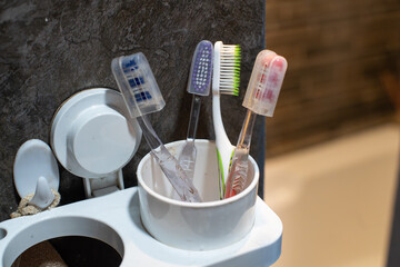colorful family toothbrushes in a white plastic holder, installed on grey ceramic-covered wall, inside a bathroom with warm lighting