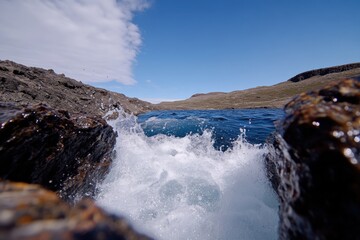 An immersive coastal scene where waves clash against rocky terrain under a clear blue sky, embodying nature&rsquo;s raw power and the majestic beauty of the seascape.