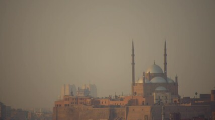 The Mosque of Muhammad Ali stands atop Cairo Citadel, its domes and towering minarets illuminated by soft haze. Modern high-rises loom in the distance, contrasting the historic fortress below. - Powered by Adobe