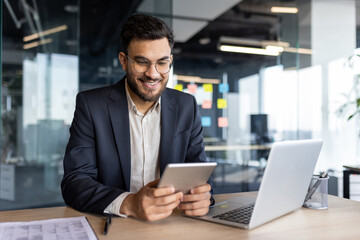 Successful businessman using tablet computer inside office at workplace. Man smiling happily, reading online financial report.