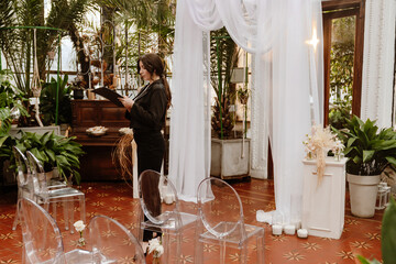 A female organizer stands and looks at a clipboard she holds in front of her, before the wedding ceremony