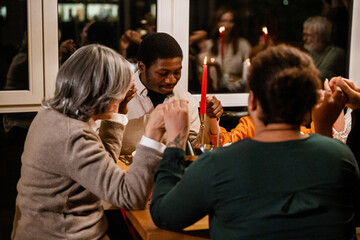 Family and guests sitting at the table and holding hands, in the living room, during Christmas dinner