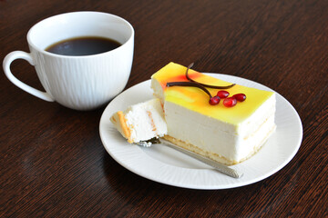 Coffee and slice of creamy cake with lemon glazing on a white plate