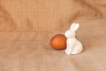 Happy easter decoration with white bunny decorative statuette and colorful eggs on eco textille background. Minimal festive composition, natural farm lifestyle. Copy space, place for text, front view