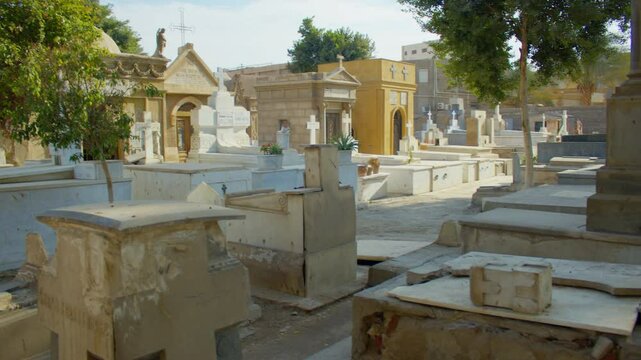 A historic cemetery with ornate mausoleums, weathered tombstones, and white crosses under a bright sky. Overview of a Coptic cemetery in Old Cairo.
