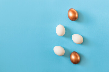 Set of Easter white and golden color eggs isolated on blue background. Stylish trendy frame composition with gold chocolate egg. Flat lay, top view, place for text. Happy egg hunt for kids concept