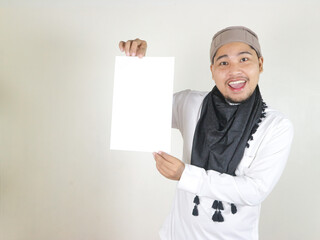 happy handsome asian muslim man wearing black turban or shemagh holding blank white paper