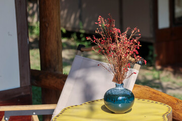 selective focus red-orange dried flowers in a blue indigo ceramic vase on a brown wooden table with...