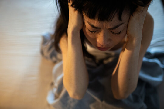 Woman sitting on bed with hands on head feeling stressed or upset