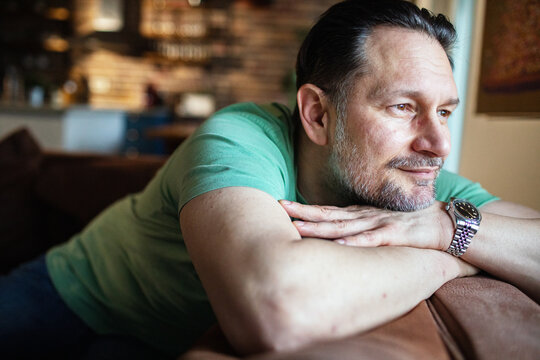 Middle aged man relaxing on couch and looking thoughtfully out the window