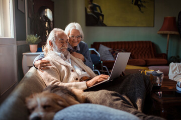 Elderly couple embracing while using laptop at home