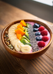 A healthy smoothie bowl topped with fresh fruit, nuts, and seeds, on a wooden table with natural light