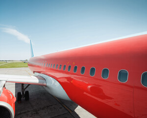 Boarding a red airplane. Perspective view of red passenger plane fuselage. Sunny day and clear sky.