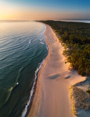 A stunning Curonian Spit beach at sunrise, with turquoise waters, soft sand, and gentle waves lapping the shore, captured from above.