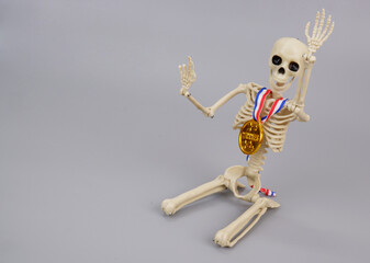 Welcoming skeleton with gold medal on gray background. Copy space for text.