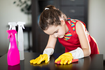 Cute little kid girl cleans table in living room at home. Child helping her mother.