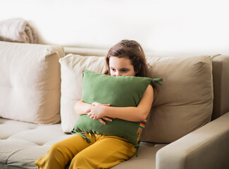 Obraz premium Child sitting alone on sofa feeling stressed unhappy, sad and depress. Little girl embracing pillow.