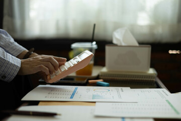 the businessman is sitting at a desk with a calculator and a stack of papers. She is looking at the papers and seems to be deep in thought
