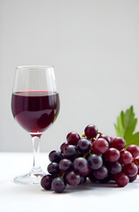 Bunches of dark ripe grapes and a glass of red wine, juice on a white table.