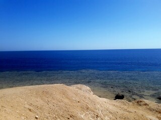 Obraz premium Panoramic View of the Ocean from a Sandy Cliff Under a Vibrant Blue Sky