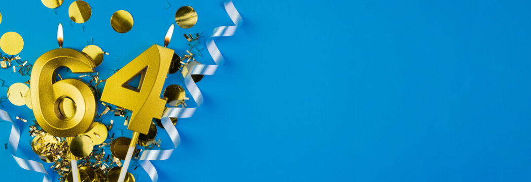 64 years celebration. Gold burning candles number sixty-four on blue background with confetti, copy space.