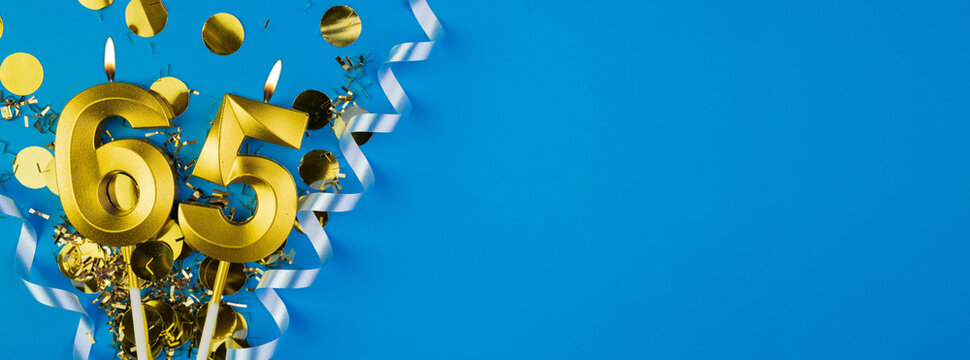 65 years celebration. Gold burning candles number sixty-five on blue background with confetti, copy space.