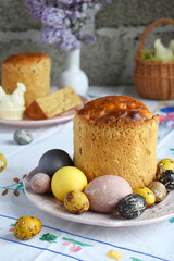 Traditional Easter Cake Decorated with Painted Eggs and Spring Flowers on Festive Table Setting. Homemade Holiday Bread Surrounded by Lilac Blooms, Quail Eggs, and Rustic Background