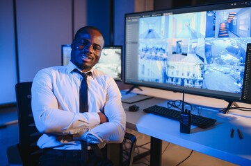 African-American security officer watching the screens talking on radio in control room